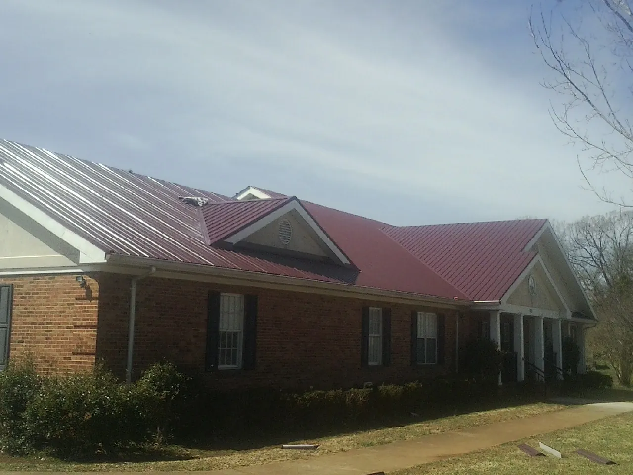 Red metal roof with gabled entries on a long brick building, from a Hail Damage Roof Repair job in Millstone Township