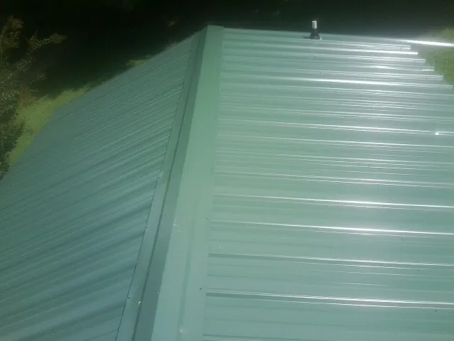 New green metal panels meeting at the ridge of a roof — Flat Roof Repair work by our crew in Millstone Township