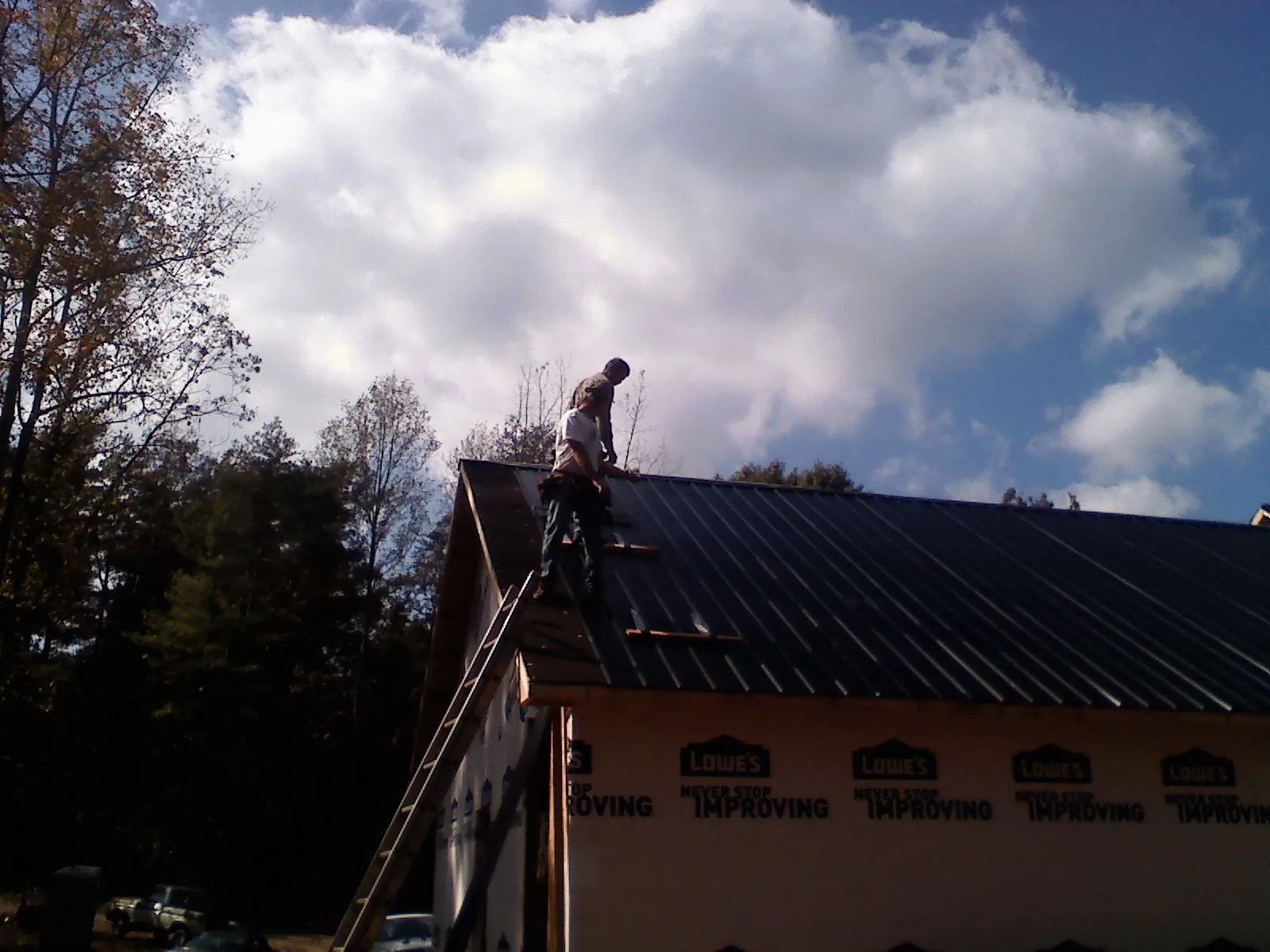 Roofer fastening dark metal panels high against a cloudy sky, from a Roof Inspection job in Millstone Township