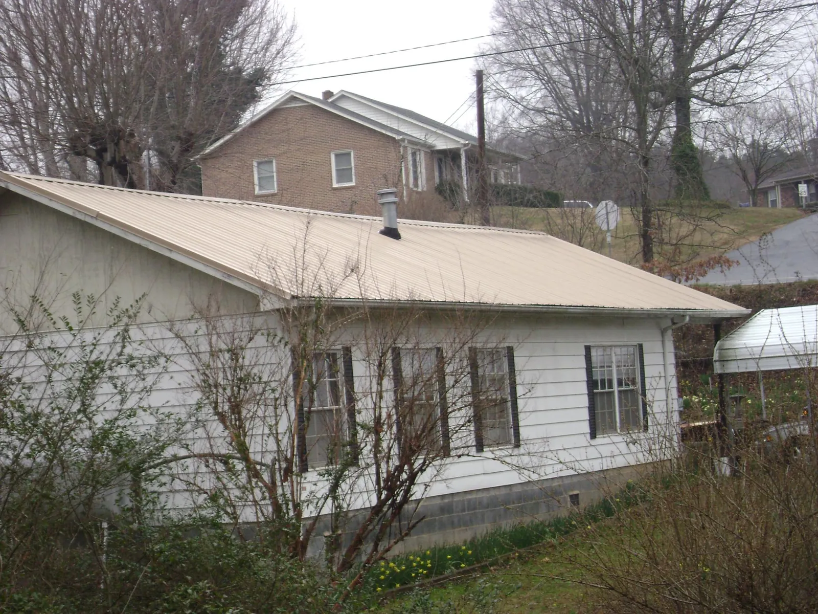 Tan metal roof on a white sided house set into a hillside — Commercial Roofing by Roofing Brothers in Millstone Township